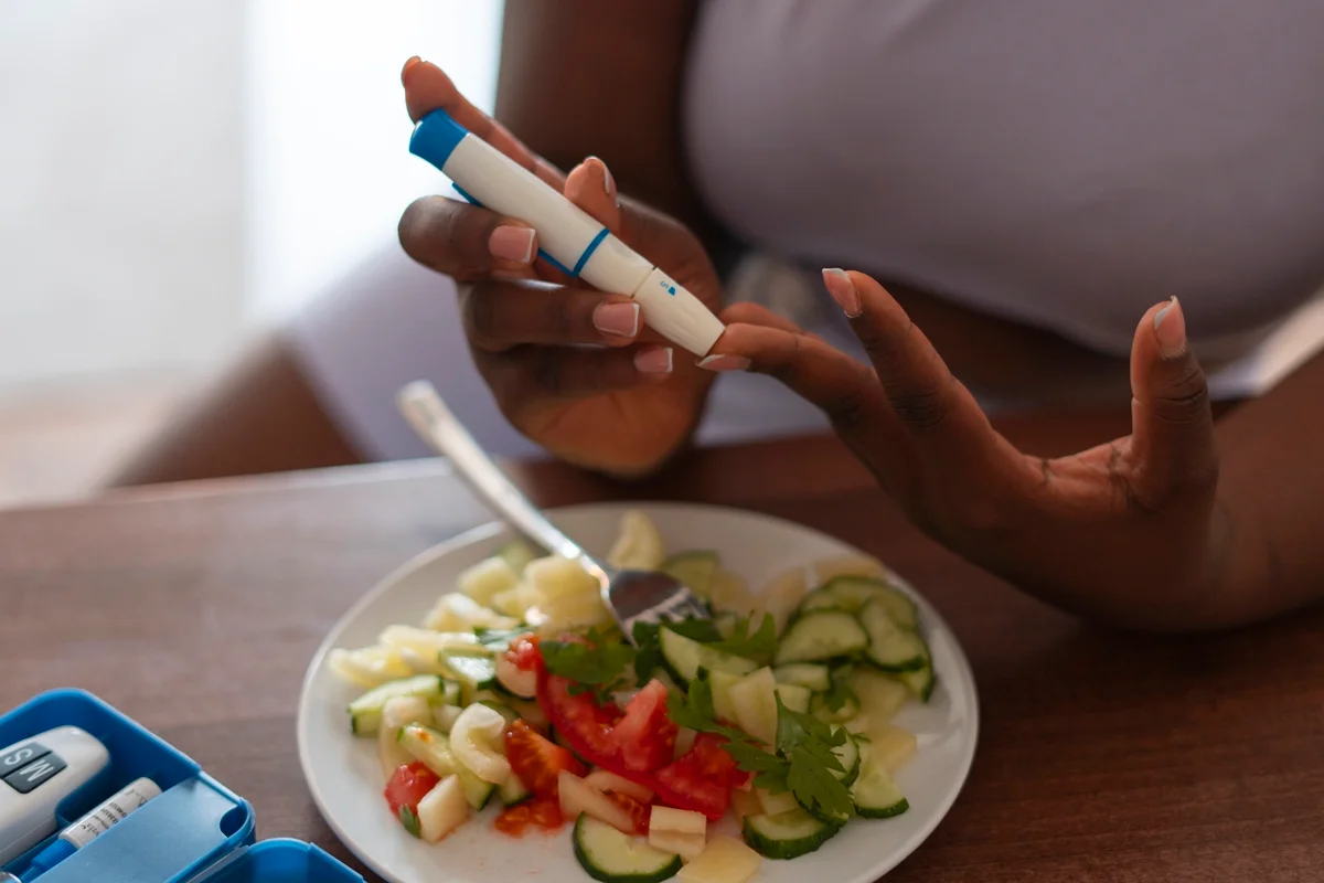 Foto colorida de mulher aplicando caneta de insulina com um prato de salada ao lado - Metrópoles